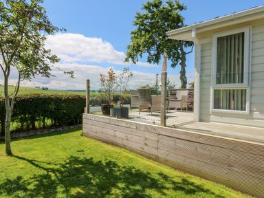 An outdoor patio with wicker chairs and glass railing next to a light-colored building at Plot 32 in High Hesket near Armathwaite