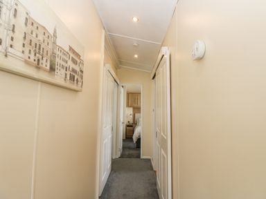 A hallway with beige walls grey carpet and white sliding doors with a painting on the left wall at Plot 32 in High Hesket near Armathwaite