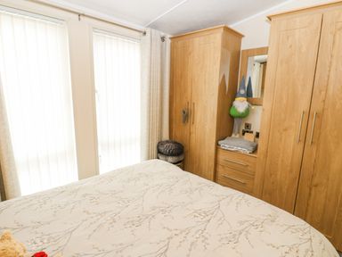 A bedroom with a bed in the foreground wooden wardrobes and a stuffed gnome in the corner at Plot 32 High Hesket near Armathwaite