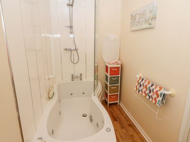 A bathroom with a bathtub shower unit wooden floor colorful drawer unit and multicolored towel at Plot 32 High Hesket near Armathwaite