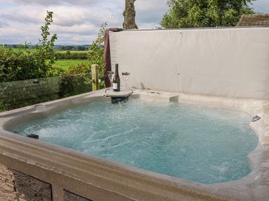 An outdoor hot tub with bubbling water and a bottle with two glasses on the edge overlooking green fields at Plot 32 High Hesket near Armathwaite