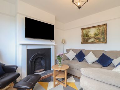A living room with a sofa, a black leather chair, a small wooden table with flowers, a fireplace, and a wall-mounted TV at The Heights in Truro