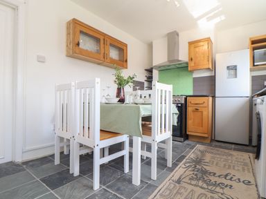 A kitchen with a dining table set with dishes and glasses white chairs wooden cabinets refrigerator and a rug on the floor at The Heights in Truro