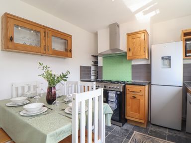 A kitchen with wooden cabinets a stainless steel refrigerator stove and a dining table set with white chairs and tableware at The Heights in Truro