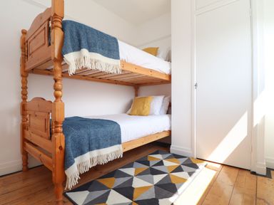 A bedroom with wooden bunk beds with blue throws yellow pillows and a geometric rug on the wooden floor at The Heights in Truro