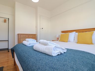 A bedroom with a wooden bed with yellow pillows folded towels on a blue blanket wooden chest of drawers and a clothes rack at The Heights in Truro