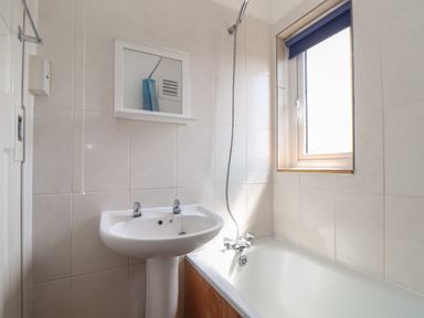 A bathroom with a white pedestal sink a bathtub with a shower and a window with a blue blind at The Heights in Truro