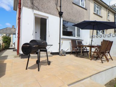 A patio with a black barbecue grill and a wooden table with chairs and a blue umbrella at The Heights in Truro