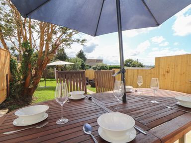 An outdoor wooden dining table with bowls forks spoons and wine glasses under a large umbrella in a garden at The Heights in Truro