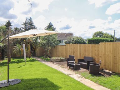 A garden with a patio umbrella and outdoor seating set along a wooden fence at The Heights in Truro