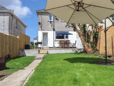 A backyard with green grass a patio table with an umbrella a barbecue and a house at The Heights in Truro
