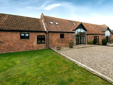A brick building with red tiled roof windows and a gravel driveway with grass area at Coot in Wheatacre