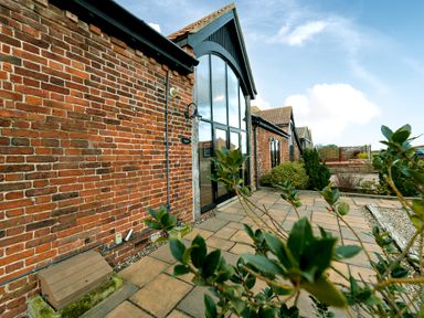 Brick building with large arched window and paved patio with plants at Coot in Wheatacre