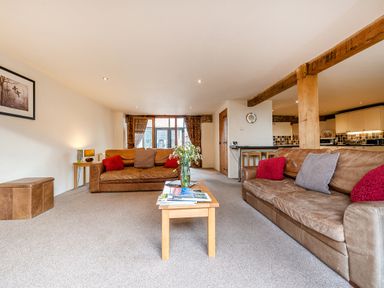 A living room with two brown leather sofas red and gray cushions a wooden coffee table with flowers and magazines and wooden beams at Coot in Wheatacre