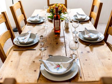 A dining table set with plates glasses cutlery napkins and a bottle of wine with flowers in the center at Coot in Wheatacre