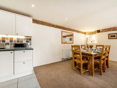 A dining area with wooden table and chairs set for six people next to a kitchen counter with cabinets at Coot in Wheatacre