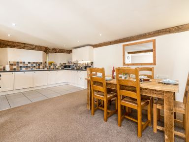 A kitchen with white cabinets and tiled backsplash next to a wooden dining table with six chairs at Coot in Wheatacre