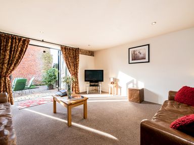 A living room with leather sofas a wooden coffee table a television and open doors leading outside at Coot in Wheatacre