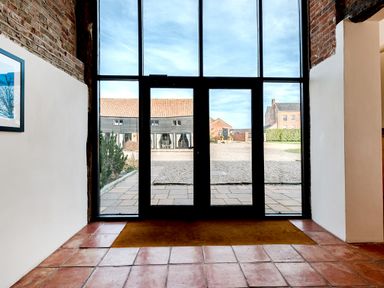 A glass door with tiled floor and brick walls leading to a courtyard with buildings at Coot in Wheatacre