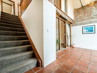 A staircase with carpet next to a tiled floor area with plants and a framed picture on the wall at Coot in Wheatacre