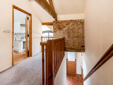A carpeted hallway with wooden railing leading to a bathroom with tiled floor and a brick wall near the staircase at Coot in Wheatacre