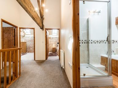 A hallway with carpet and wooden beams leading to two bedrooms and a bathroom at Coot in Wheatacre