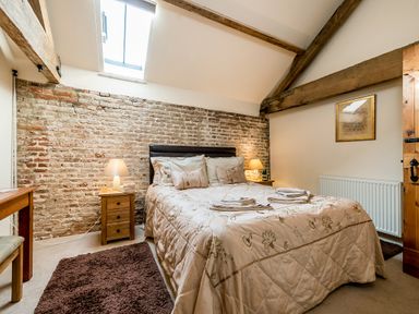A bedroom with a double bed pillows bedside tables lamps exposed brick wall wooden beams and a skylight at Coot in Wheatacre
