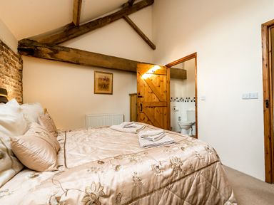 A bedroom with a bed towels wooden beams and an open door showing a toilet at Coot in Wheatacre