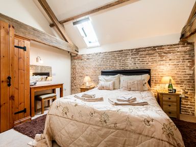 A bedroom with a double bed bedside tables a dressing table wooden beams and a skylight window at Coot in Wheatacre