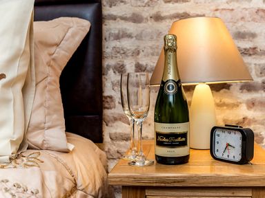 A bedside table with champagne bottle two glasses a lamp and a clock next to a bed at Coot in Wheatacre