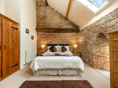 A bedroom with exposed brick walls a double bed two bedside tables with lamps and a wooden wardrobe at Coot in Wheatacre