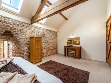 A bedroom with a bed a brown rug a wooden dresser and a wooden dressing table with a stool at Coot in Wheatacre