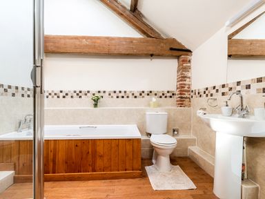 A bathroom with a bathtub wooden paneling exposed wooden beams a toilet a pedestal sink and tiled walls at Coot in Wheatacre