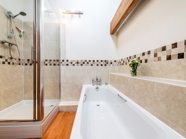 A bathroom with a shower enclosure and a bathtub with tiled walls and a wooden beam at Coot in Wheatacre