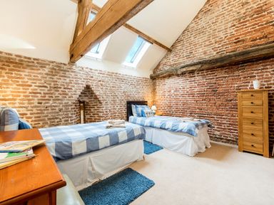 A bedroom with two single beds blue checkered bedding wooden chest of drawers and exposed brick walls at Coot in Wheatacre