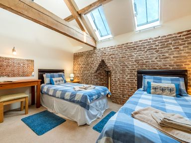 A bedroom with two single beds with blue checkered bedding a wooden table with a mirror and a stool exposed brick walls and skylights at Coot Wheatacre