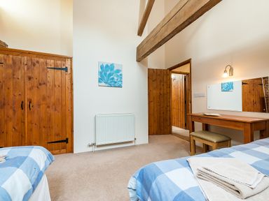 A bedroom with two single beds covered in blue checkered bedding a wooden dressing table with a stool a large mirror wooden doors and exposed ceiling beams at Coot in Wheatacre