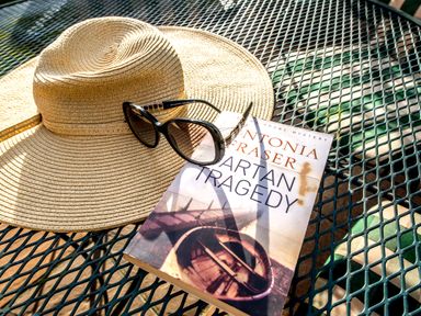 A straw hat sunglasses and a book titled Spartan Tragedy on a metal outdoor table at Coot in Wheatacre
