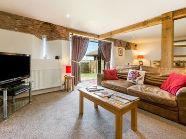 A living room with a brown leather sofa and coffee table facing a television at Widgeon in Wheatacre