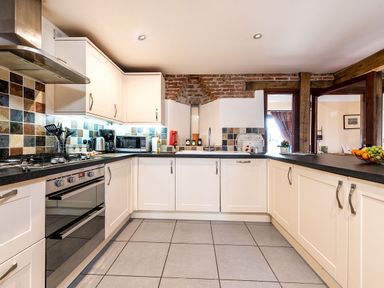 A kitchen with white cabinets a tiled backsplash a built in oven a microwave and a sink at Widgeon in Wheatacre
