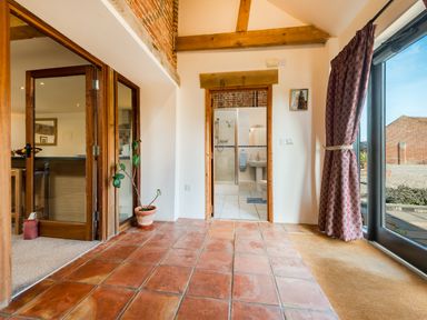 A tiled hallway with a potted plant and doorway leading to a bathroom with glass shower at Widgeon in Wheatacre