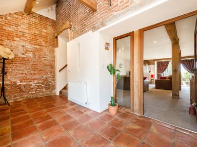 An entrance area with terracotta tile flooring exposed brick walls a staircase a coat rack a potted plant and a living room visible through wooden framed glass doors at Widgeon in Wheatacre