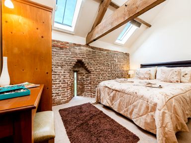 A bedroom with a bed a wooden desk and exposed brick wall with skylights at Widgeon in Wheatacre