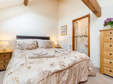 A bedroom with a bed and bedside tables with lamps a wooden chest of drawers and an open door to a bathroom at Widgeon in Wheatacre