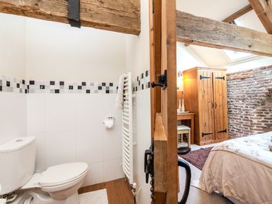 A bathroom with a toilet and a radiator next to a bedroom with a wooden wardrobe and a desk at Widgeon in Wheatacre