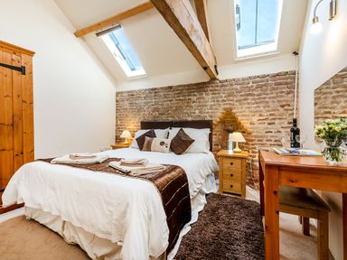 A bedroom with a bed table lamps a wooden wardrobe and a desk with flowers at Widgeon in Wheatacre