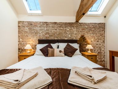 A bedroom with a double bed two bedside tables with lamps exposed brick wall and skylights at Widgeon in Wheatacre