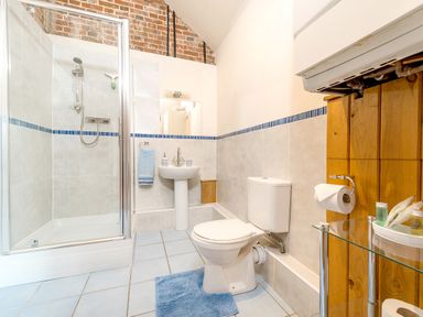 A bathroom with a shower, toilet, pedestal sink, blue rug, and wooden paneling at Widgeon in Wheatacre