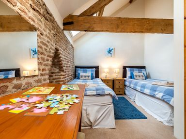A bedroom with two single beds a wooden table with puzzles exposed brick wall and wooden ceiling beams at Widgeon in Wheatacre