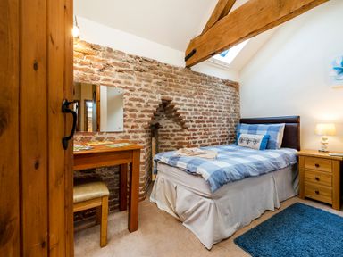 A bedroom with a single bed a wooden desk and chair a brick wall with a small alcove and wooden beams at Widgeon in Wheatacre
